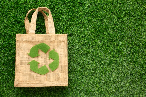 Eco-friendly jute bag with a green recycling symbol placed on lush green grass, symbolizing sustainability and environmental consciousness.